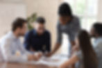 Black woman leading a team meeting, leaning over the table while explaining key information in a modern conference room.
