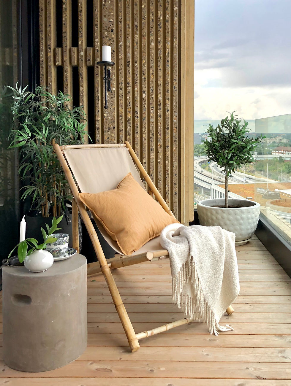 Solstol i canvas och bambu med kudde och filt på liten balkong med betongbord bredvid
