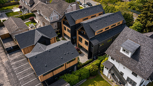 Aerial hero view of Ansoku showing the multiplex massing, pitched roofs, cedar and black material palette, and surrounding homes.