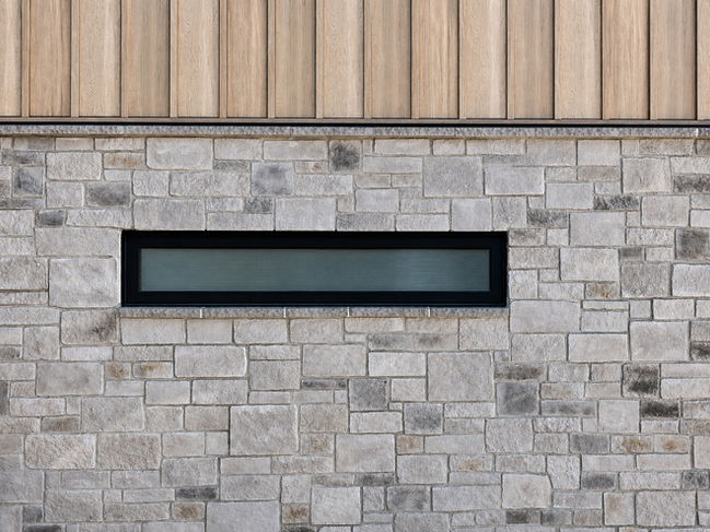 Material detail at Japavarian Haus by Longpre Architecture, showing stone cladding, black framed horizontal window, and warm vertical wood siding.