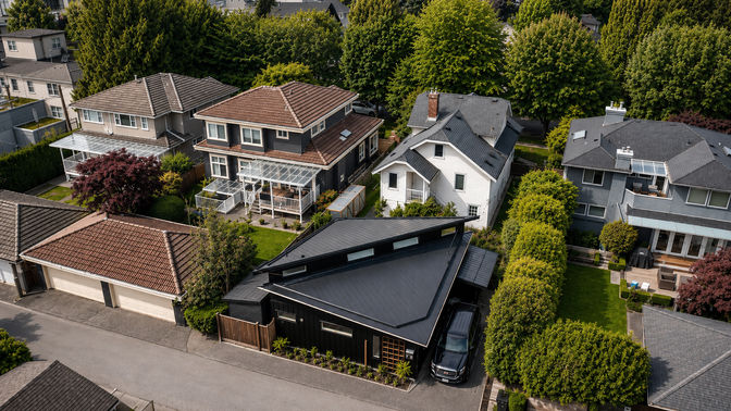 Aerial view of Japavarian Blades laneway home with black roof, patio, garden, hedge, and surrounding Vancouver houses.