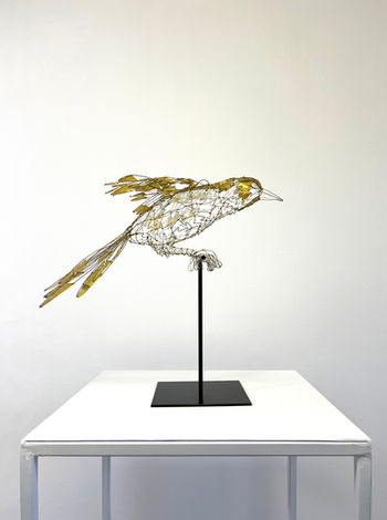 Sculpture d'une pie en fil et feuilles de laiton, posée sur un socle