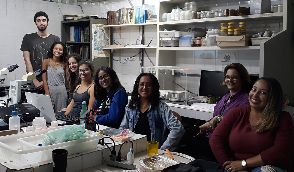 toda a equipe sentada lado a lado em torno de uma bancada com microscópios e outros equipamentos de laboratório