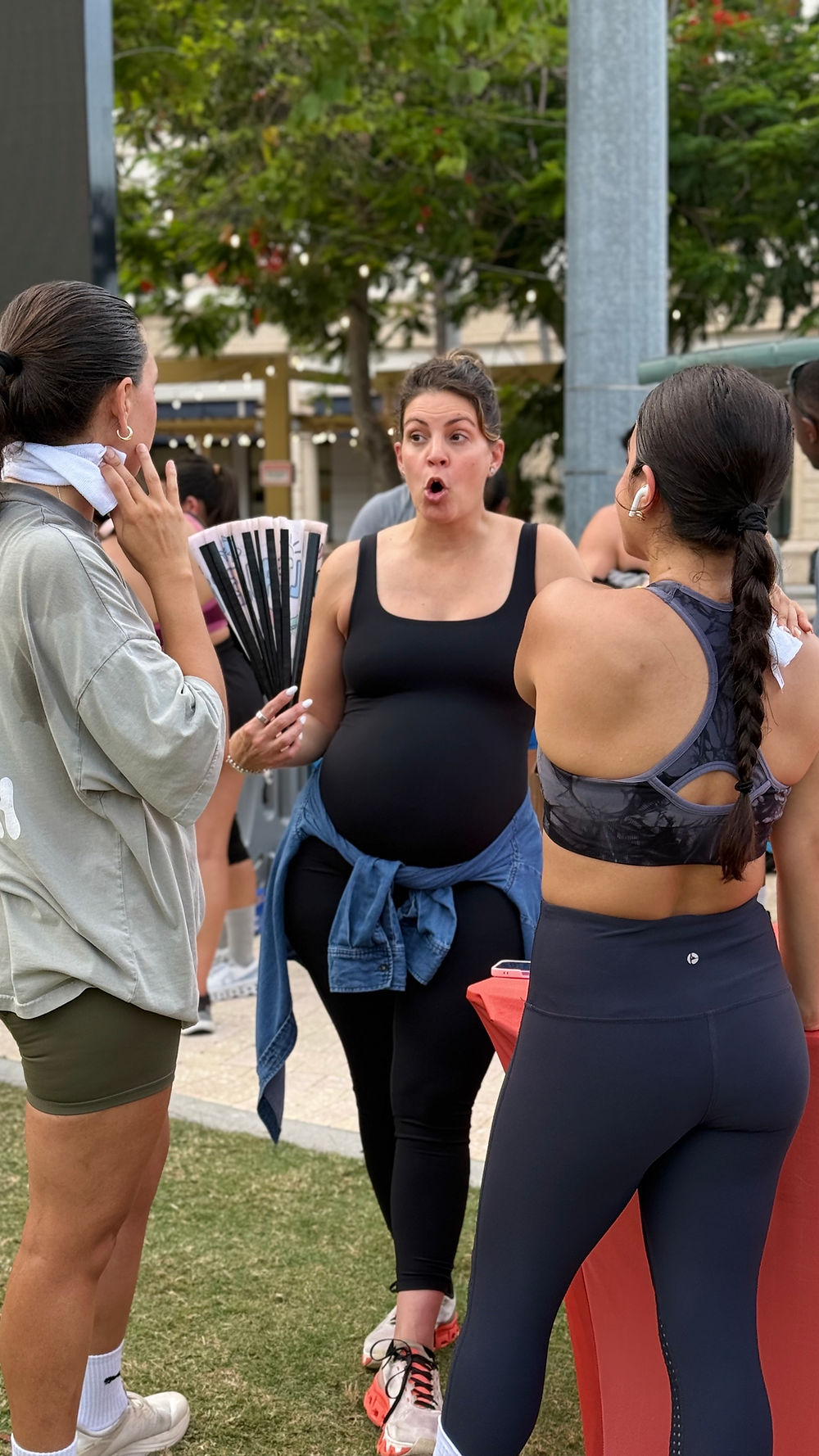 A pregnant provider having an animated, friendly conversation with two attendees at the SoléMar Psychiatry booth during an outdoor community wellness event.