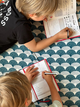 Child writing in the Ik boek on patterned surface