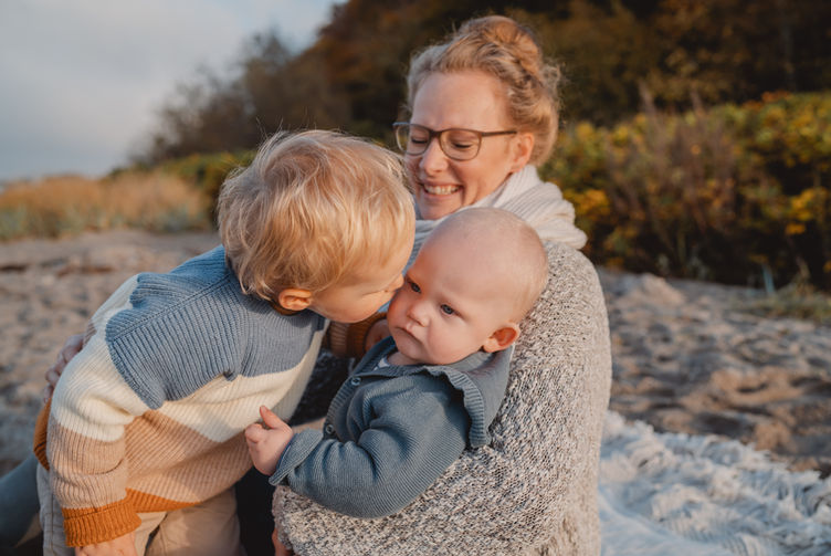 Mutter mit zwei Kindern. Kinder geben sich einen Kuss.