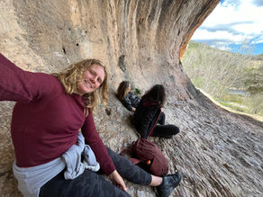 Three people resting inside the large rock shelter of Cova Negra in Xàtiva, surrounded by natural stone formations with views of trees and the outdoor landscape beyond the cave opening.
