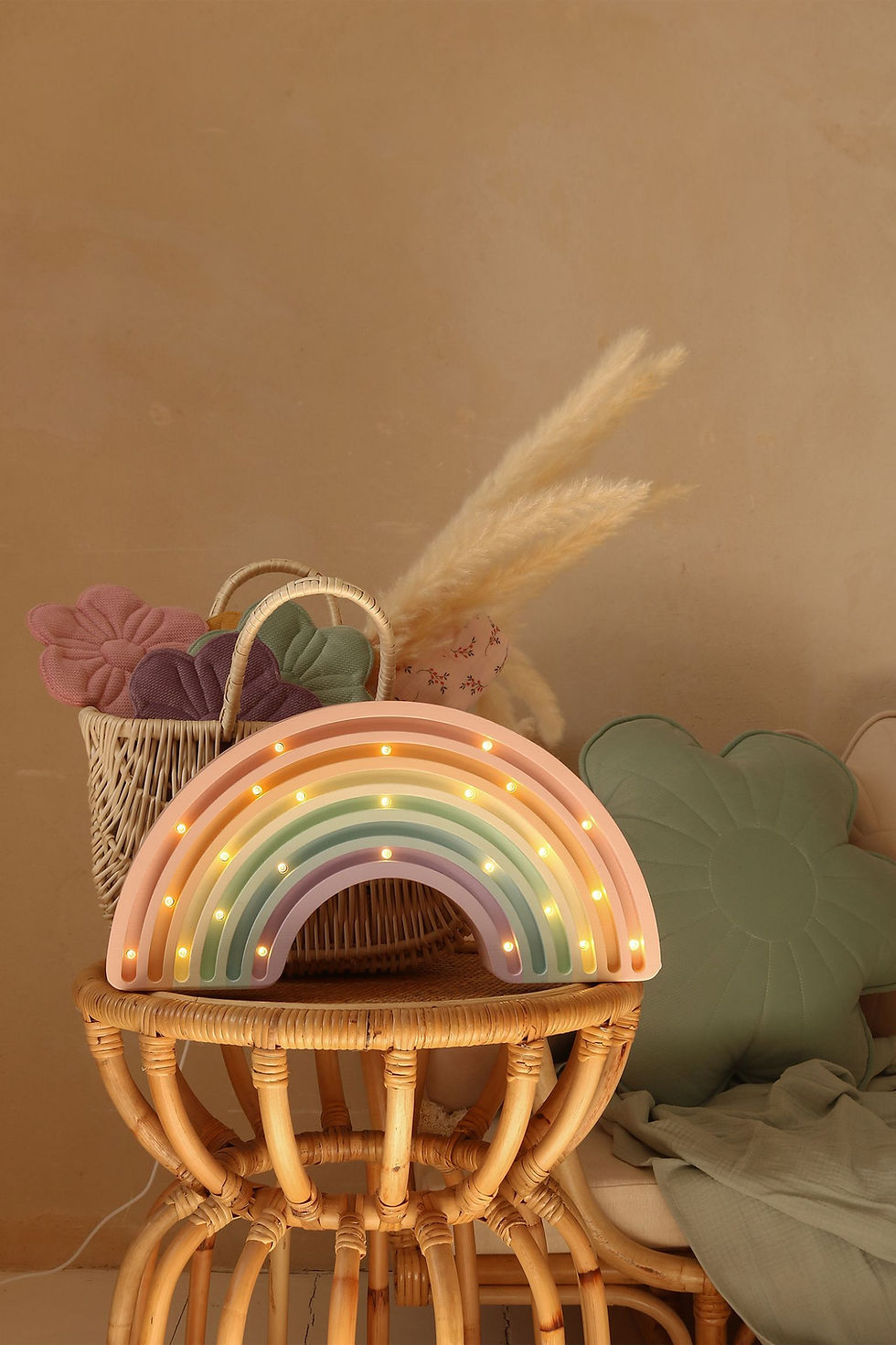 houten kinderlamp in de vorm van een regenboog in pastel kleuren op een rotan tafeltje