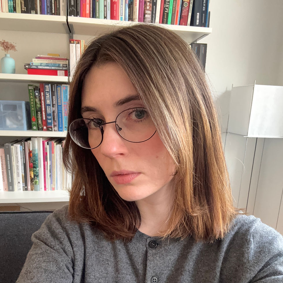 Jill Blackmore Evans wearing glasses and brown hair poses in front of a bookshelf. She's wearing a gray top, and the setting is a cozy, well-lit room.