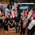 A diverse group of students from Oasis Skateboard Factory holds colorful skateboards with unique designs inside their classroom. Visible signs read "GRACIOUS CRUNCH" and "HUSH MODE." Smiling faces.