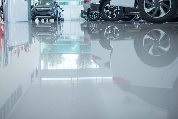Modern beautiful showroom with cars being sold. The underside of a car is reflected by th