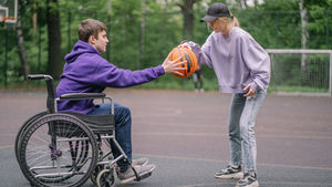 A young man in a wheelchair enjoying basketball outdoors with a friend, reflecting an NDIS day respite activity.