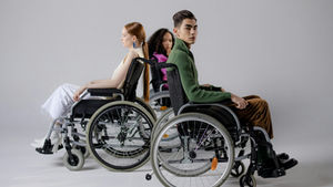 Three diverse individuals in wheelchairs posing indoors, symbolizing inclusivity.