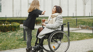 A joyful moment of a mother in a wheelchair bonding with her daughter in a park.