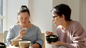 Two women sharing breakfast, one with Down syndrome, fostering togetherness and care.