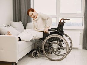 A woman with dyed short hair smiles while transitioning from a wheelchair to a couch.