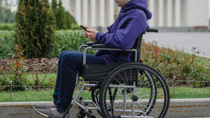 Young man in wheelchair using a cellphone near a building, representing self-advocacy and escalating concerns about respite service quality.