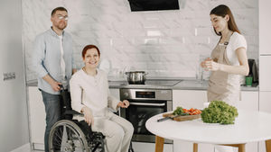 Three adults enjoying family time preparing food in a bright kitchen.