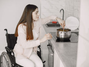 Woman in a wheelchair stirring a pot on the stovetop in a modern kitchen, reflecting NDIS Assistance with Daily Living support.