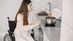 Woman in a wheelchair stirring a pot on the stovetop in a modern kitchen, reflecting NDIS Assistance with Daily Living support.