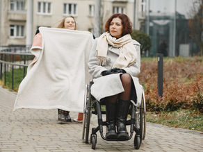 Woman in a wheelchair with a child holding a blanket outdoors on a cobblestone path.