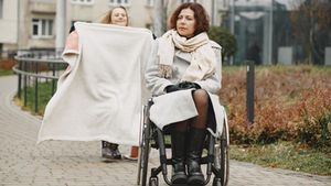 Woman in a wheelchair with a child holding a blanket outdoors on a cobblestone path.