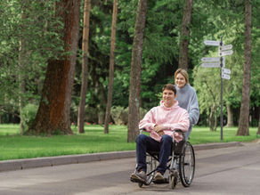 Happy couple enjoying a sunny day outdoors, with a woman pushing a man in a wheelchair.