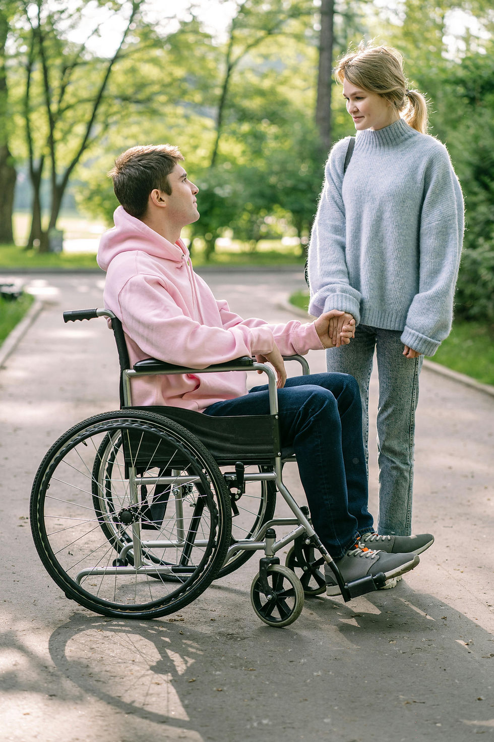 Young couple holding hands outdoors with one in a wheelchair, representing trust and safe support in risk-assessed respite environments.