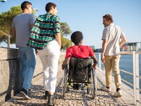 Diverse group of friends walking by a river, including one person in a wheelchair.