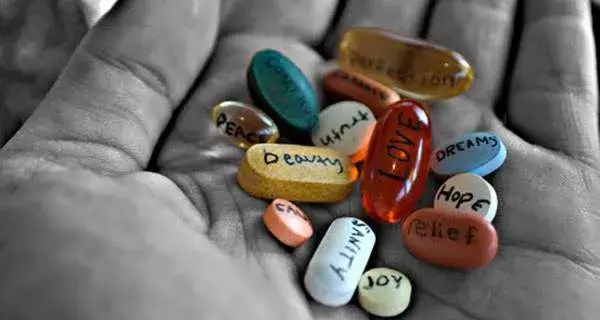 Una mano aperta raffigurata in bianco e nero, tiene una serie di pillole colorate. I farmaci in questione porterebbero bellezza, amore, verità, pace, salute, felicità, sollievo, speranza.. Si tratta di una provocazione contro la tendenza attuale a medicalizzare tutto