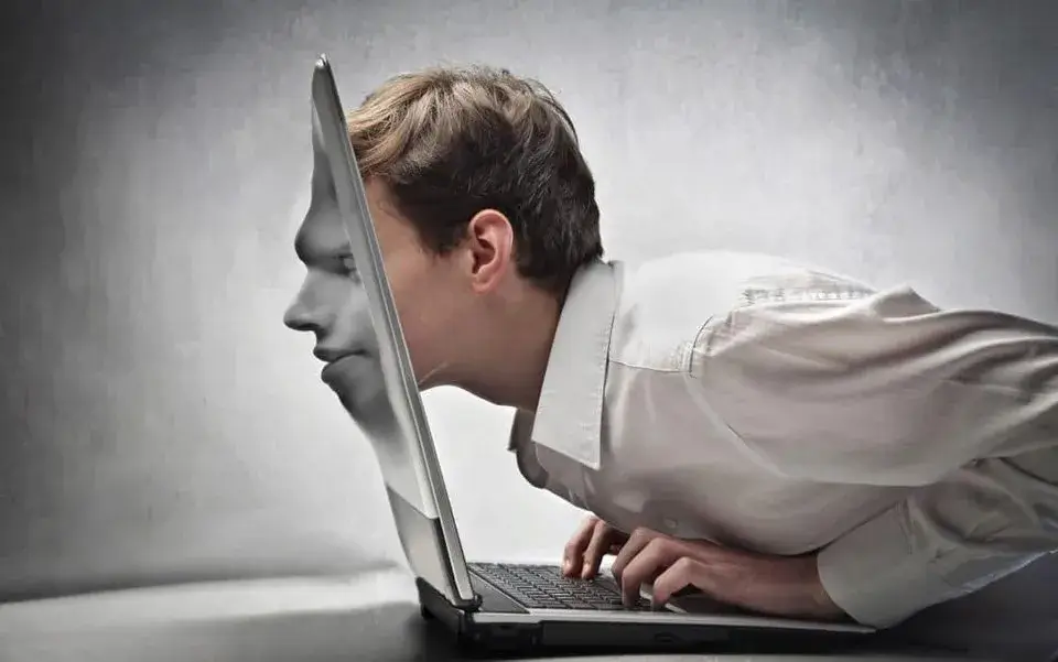 Immagine che ritrae un uomo mentre scrive al computer e entra nello schermo del computer, perdendo i confini tra realtà virtuale e non.