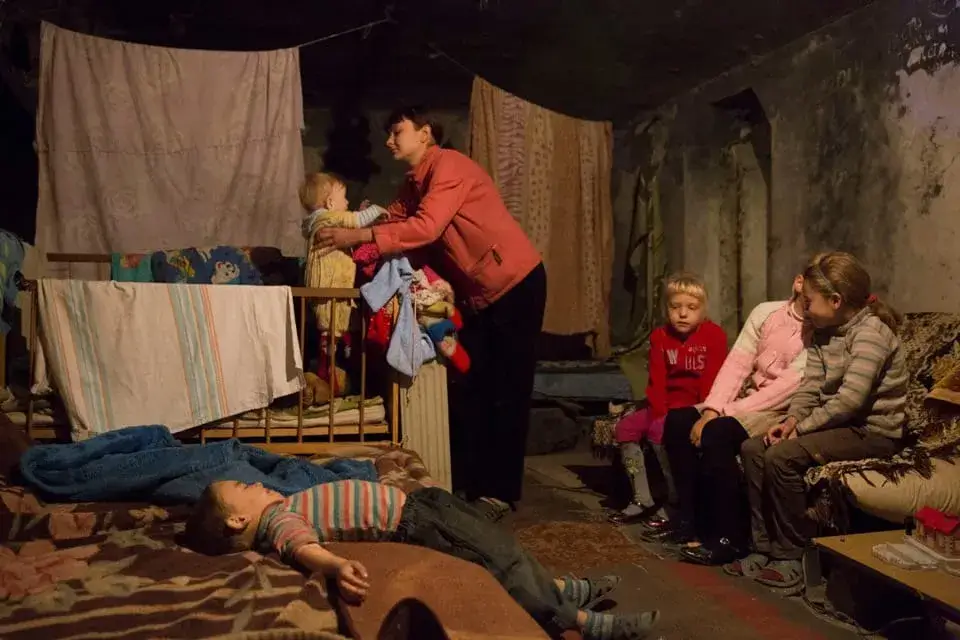 La fotografia scattata nel 2023 in Ucraina, teatro della guerra scoppiata a seguito dell'invasione Russa. Si vede una famiglia povera materialmente. Le pareti della stanza sono piene di muffa, numerosi lenzuoli sono stesi nel tentativo di farli asciugare. La madre si prende cura del bambino più piccolo, mentre gli altri sembrano esausti, tristi, sconsolati.