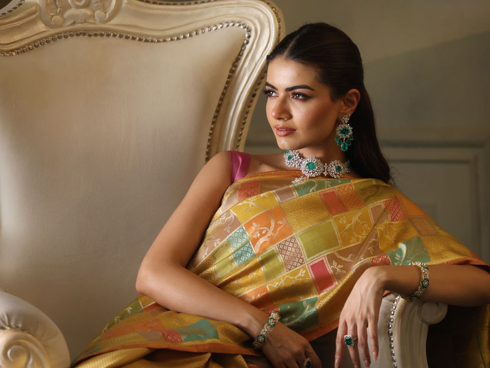 Woman in gold patterned sari and emerald jewelry sits on ornate chair