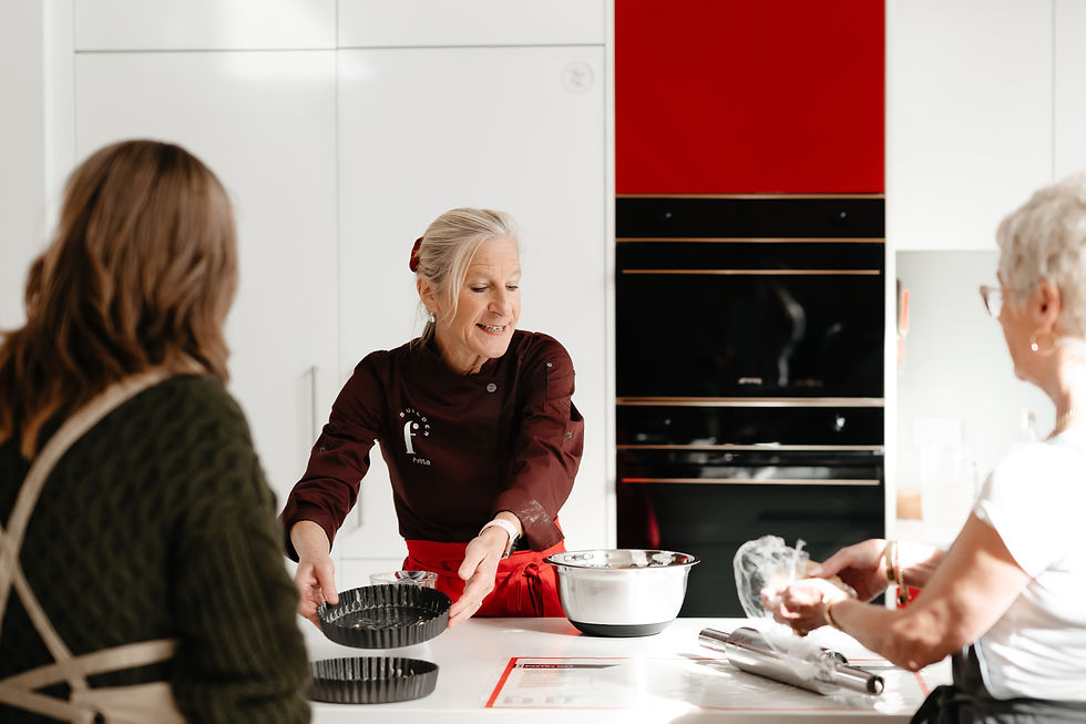 Anita Robin in the kitchen in between 2 of her students teaching a class