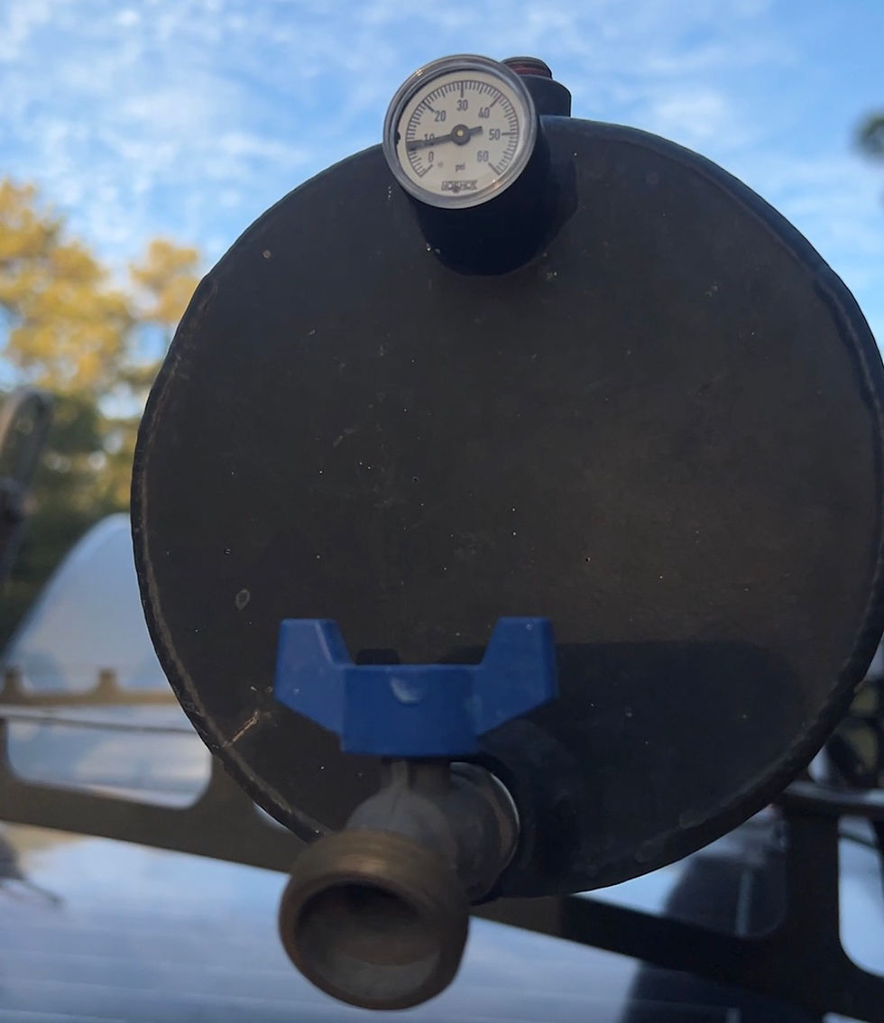 Close-up of a black cylinder water tank with a pressure gauge and blue water valve against a blue sky.