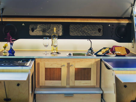 Compact and custom galley kitchenette with sink, wine bottle, two glasses, flowers, and food trays on a tidy and elegant Pindrop counter
