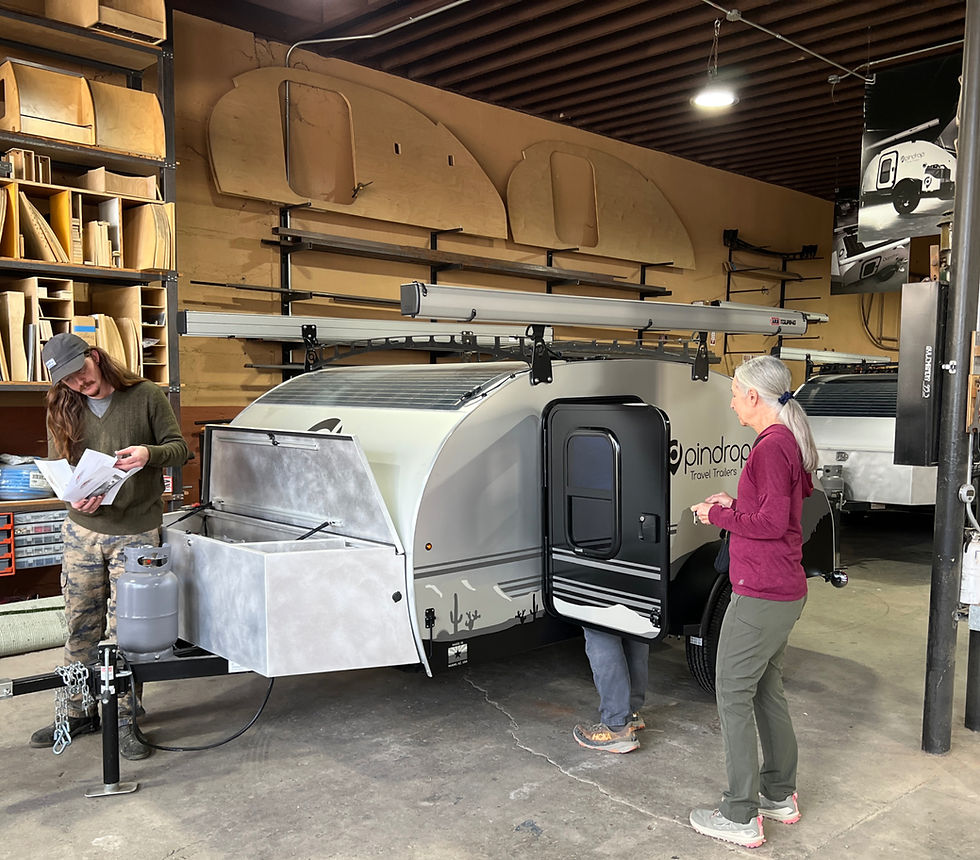 Customers receiving VIP attention when Picking up a Pindrop travel trailer in a workshop, with shelves of wood and trailer parts on the walls.