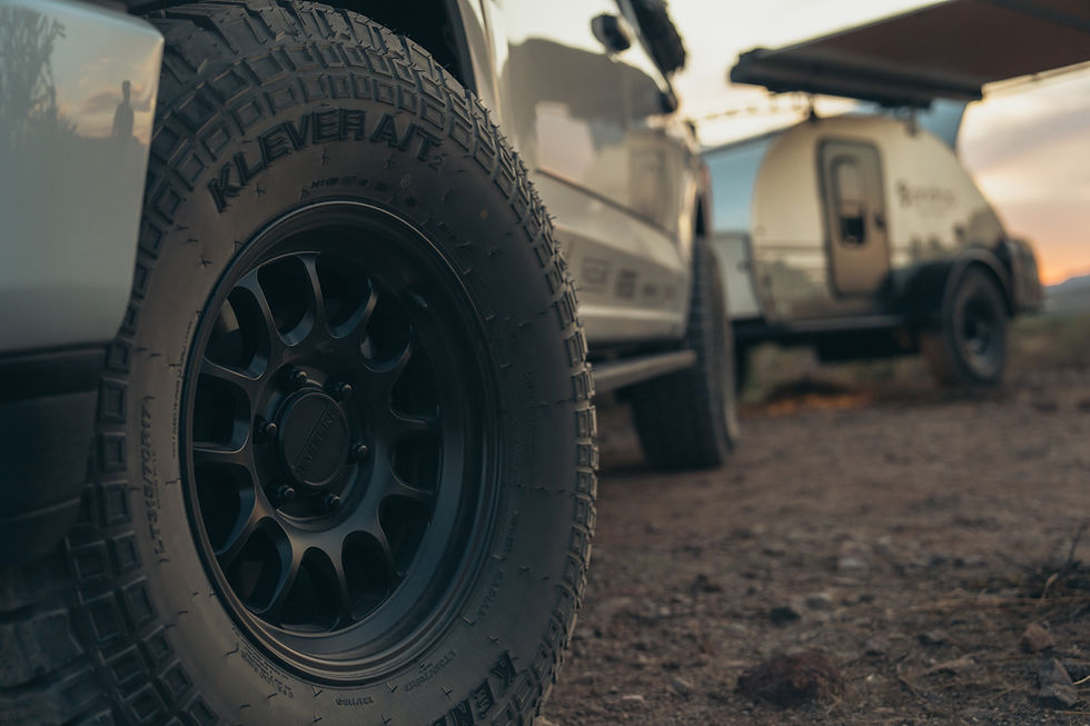 A close up of a Raceline tire, with black rim and rugged design. A pindrop trailer is faded in the background at dusk.