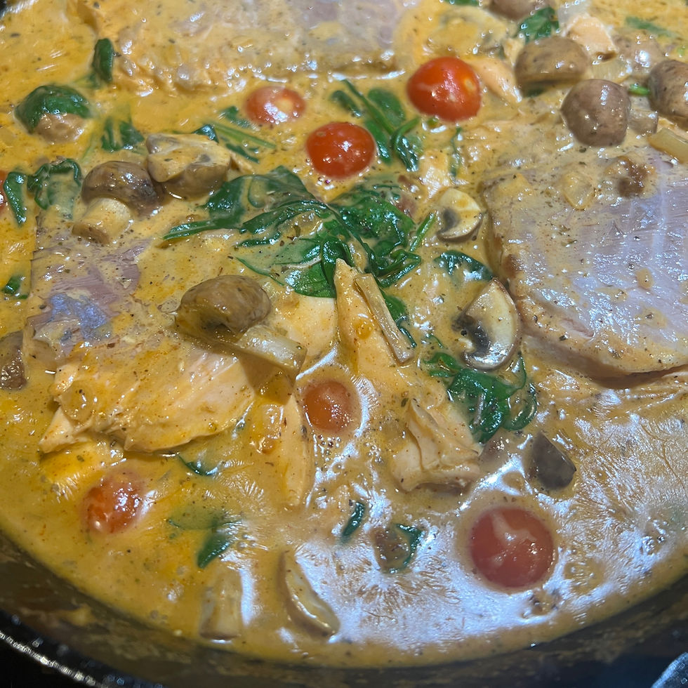 A creamy dish in a pan with mushrooms, spinach, cherry tomatoes, and chicken in a rich yellow sauce, creating a hearty and warm meal.