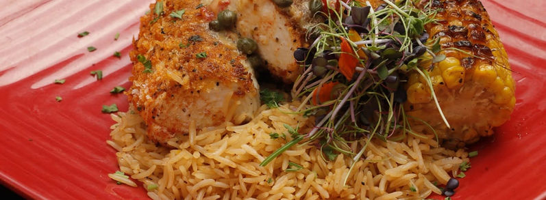 Grilled fish served over seasoned rice with corn and microgreens