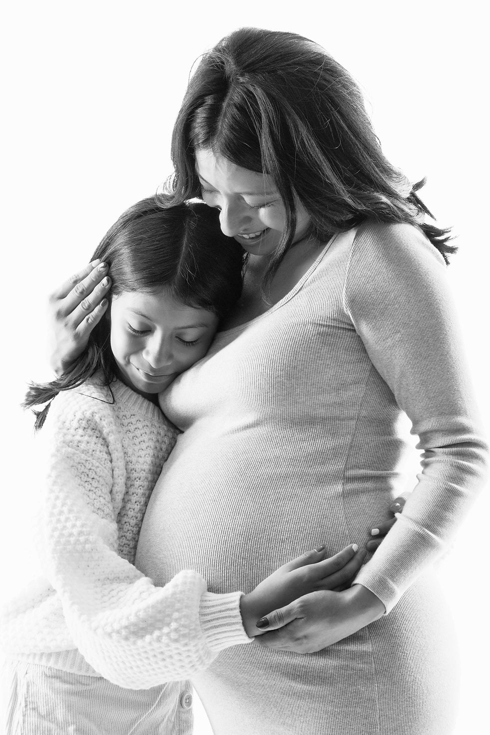 Pregnant woman in a soft-lit NYC studio during a maternity photoshoot at Tals Studio, wearing flowing fabric and smiling confidently.