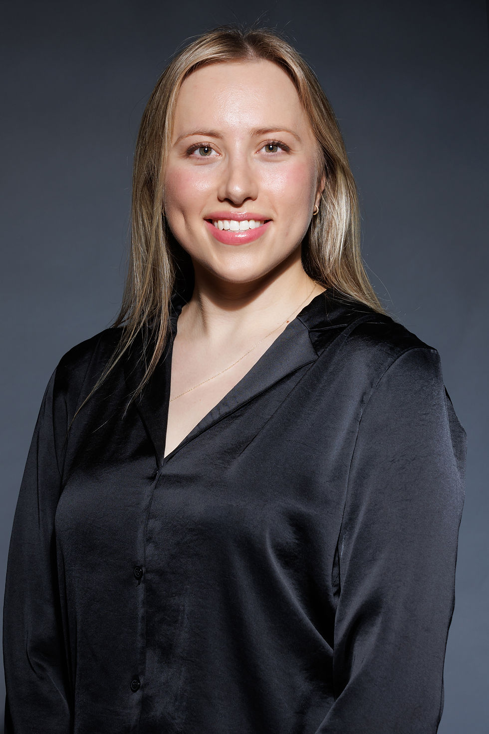 Portrait showing the torso and head of a woman wearing a black satin shirt against a dark gray background.