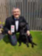 Photo of John Davidson holding his MBE medal and his black labrador Suki