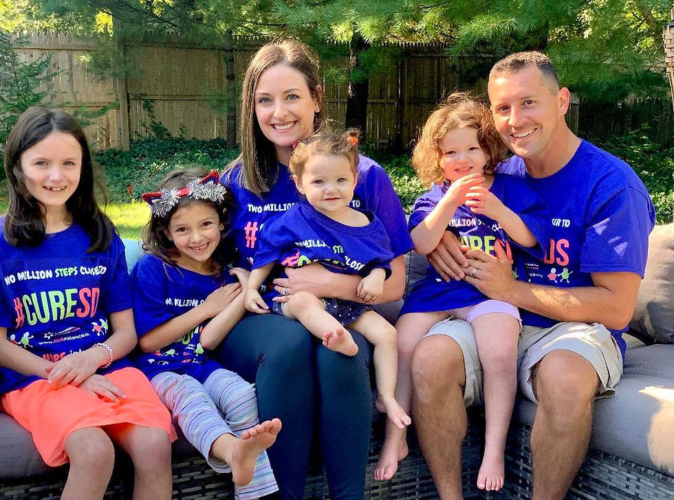 A proud SDS family (mom, dad, and 4 young daughters) sporting their vibrant blue T-shirts, sitting outdoors, smiling, and looking into the camera, in support of SDS research, ready for the Two Million Steps Closer to #CureSDS challenge!