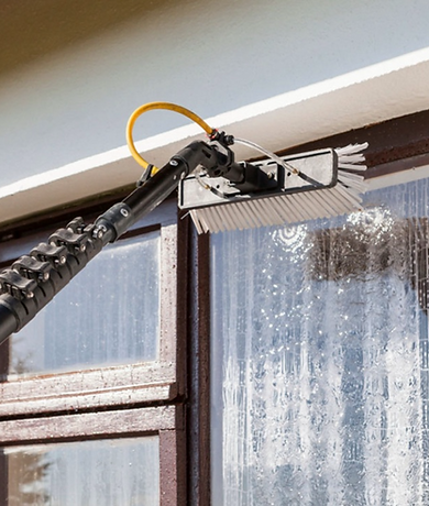 A professional using a water-fed brush to clean a window, removing dirt and grime with purified water for a spotless, streak-