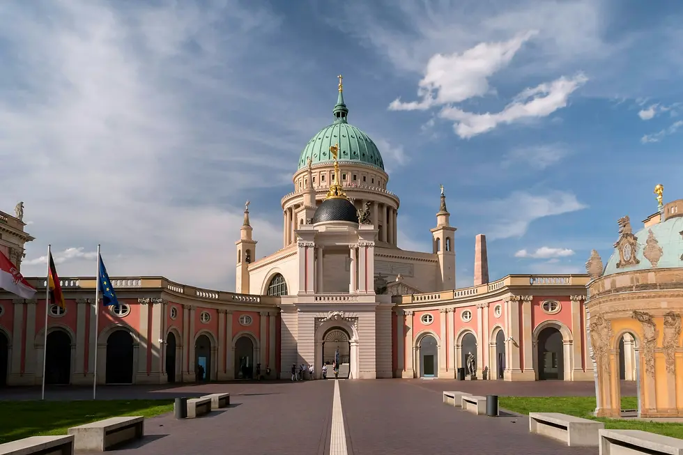 Pink neoclassical domed church with a green cupola and flags under a partly cloudy sky, private jet catering at Schönhagen Airfield (QXH / EDAZ), Trebbin, Germany