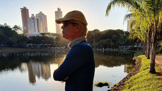 Homem olhando o horizonte, em ambiente urbano, com um lago no fundo e céu azul