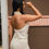 Thumbnail: Mulher em vestido branco posando; Melanina, fundo marrom e parede clara.