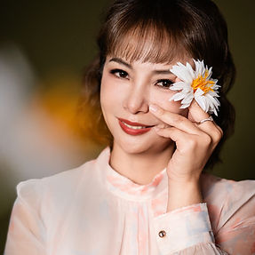 一位女士拿著一朵花，遮住一隻眼睛，微笑著，形象照。