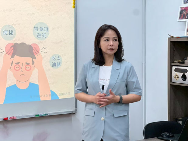 一位女士站在讲台前,旁边有文字和图画,中华华梵美容美體保健協會。